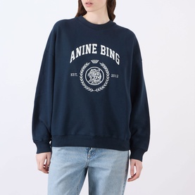 Model wearing Anine Bing Miles Collegiate Logo Sweatshirt in navy with white crest graphic, round neck, dropped shoulders, styled with light-wash