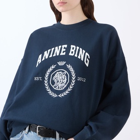 Model wearing Anine Bing Miles Collegiate Logo Sweatshirt in navy with white crest print, styled with black belt and jeans.