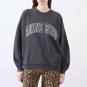 Model wearing Anine Bing Miles Logo Sweatshirt in Washed Black with arc logo print, crew neck, dropped shoulders, styled with leopard print trousers.