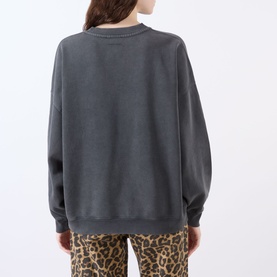 Model wearing Anine Bing Miles Logo Sweatshirt in Washed Black, back view, with leopard-print trousers. Dropped shoulders, ribbed trims, 100% cotton.