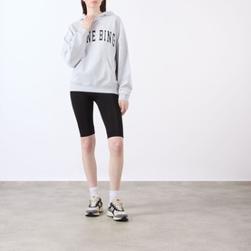 Model wearing Anine Bing Harvey New Classic Hoodie in grey melange with black cycling shorts and multicolour trainers.