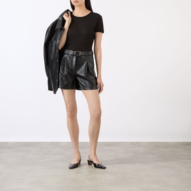 Model wearing Anine Bing black short-sleeve top, styled with black leather shorts, belt, and black kitten heel mules; draping jacket over shoulder.
