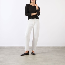 Model wearing Anine Bing black long-sleeve top in lyocell-wool blend, styled with white straight-leg jeans and black flat mules.