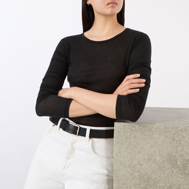 Model wearing Anine Bing black long-sleeve top in lyocell-wool blend, styled with white wide-leg trousers and a white belt.