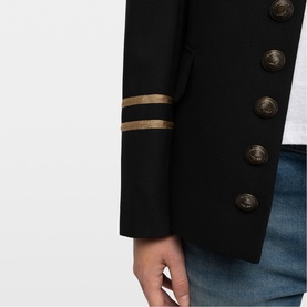 Model wearing Zadig black military-style blazer with gold stripe cuff detail and gold-tone buttons, styled with blue jeans.