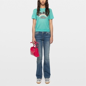 Model wearing Zadig green graphic T-shirt with rainbow print, styled with blue flare jeans, carrying small pink handbag