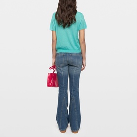 Model wearing Zadig green short-sleeve T-shirt, styled with blue flare jeans and carrying a small red structured bag.