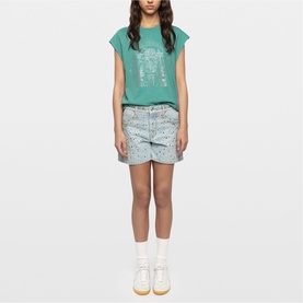 Model wearing Zadig green graphic T-shirt styled with light blue paint-splatter denim shorts and white socks with yellow trainers.
