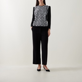 Model wearing Caroline Kilkenny white and black geometric print top with long sleeves, styled with black wide-leg trousers and heels.