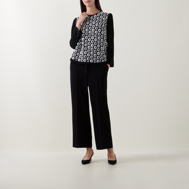 Model wearing Caroline Kilkenny white and black geometric print top with long sleeves, styled with wide-leg black trousers and black pumps.
