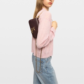 Model carrying Zadig purple small crossbody bag with gold chain strap, styled with pink knit top and light blue jeans
