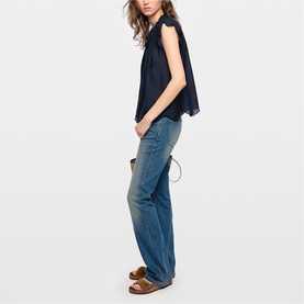 Model wearing Zadig blue sleeveless flared top with mid-blue wide-leg jeans and tan sandals, side profile view.