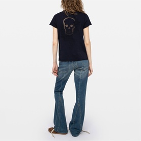 Model wearing Zadig blue T-shirt with skull graphic on back, styled with flared denim jeans and tan sandals