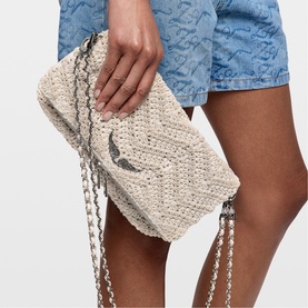 Model carrying Zadig white woven raffia clutch bag with silver chain straps and bird charm detail
