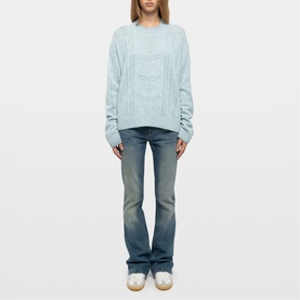 Model wearing Zadig blue cable-knit crew-neck sweater, styled with light-wash flared jeans and white trainers.