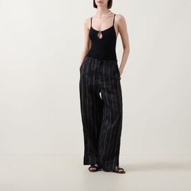 Model wearing Hunza G Toni Textured One-Piece Swimsuit in Metallic Rosewood with wide-leg striped trousers and brown sandals.