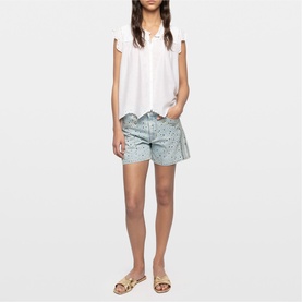 Model wearing Zadig white sleeveless top with ruffle trim, styled with light blue printed shorts and gold sandals.