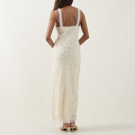 Model wearing LOVESHACKFANCY Lemon Haze floral maxi dress with lace trim straps and hem, back view, styled with gold sandals