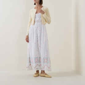 Model wearing LOVESHACKFANCY Optic White cotton maxi dress with floral embroidery, styled with cream cropped cardigan and yellow ballet flats.