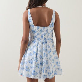 Model wearing LOVESHACKFANCY Nabi Floral Print Mini Dress in Blue Marina, showing smocked back, wide straps and flared skirt. Styled with pearl