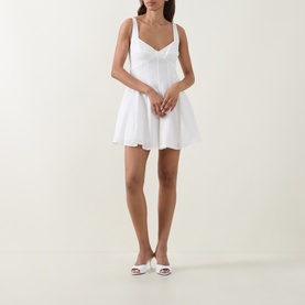 Model wearing LOVESHACKFANCY white linen mini dress with sweetheart neckline, fitted bodice and flared skirt, styled with white heeled mules.