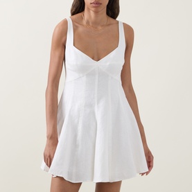 Model wearing LOVESHACKFANCY white linen mini dress with sweetheart neckline, wide straps, and fit-and-flare silhouette.