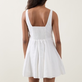 Model wearing LOVESHACKFANCY white linen mini dress, rear view showing square neckline, smocked back bodice and flared skirt.