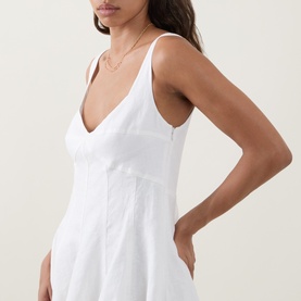 Model wearing LOVESHACKFANCY white linen dress with V-neckline, thin straps, and fitted bodice with seam detailing.