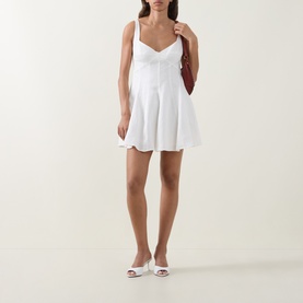 Model wearing LOVESHACKFANCY white linen mini dress with sweetheart neckline and flared skirt, styled with white mule heels and red shoulder bag.