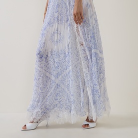 Model wearing LOVESHACKFANCY Indigo Shores silk dress with floral lace overlay in blue and white, styled with white heeled mules.