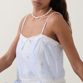 Model wearing LoveShackFancy Sky Mist cotton dress with lace trim and spaghetti straps, styled with a pearl choker necklace.