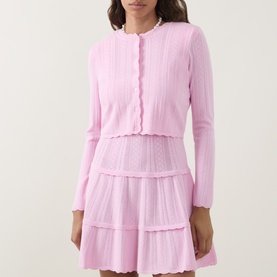 Model wearing LOVESHACKFANCY Candy Floss Pink knit cardigan with scallop trim, styled with matching tiered mini skirt and pearl necklace