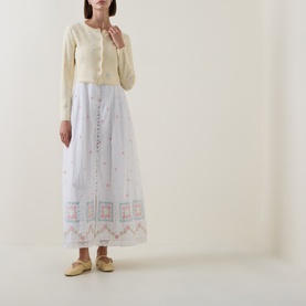Model wearing LoveShackFancy Dayly cropped knit cardigan, styled with white embroidered maxi skirt and cream flat shoes