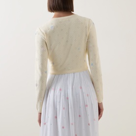 Model wearing LOVESHACKFANCY Dayly knitwear, cream with floral embroidery, styled with a white polka dot pleated midi skirt, back view.