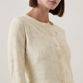 Model wearing LOVESHACKFANCY Dayly cardigan in cream with floral embroidery, eyelet detailing, and button front fastening.