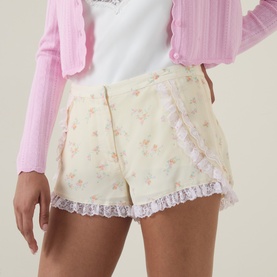 Model wearing LOVESHACKFANCY Lemon Haze floral viscose shorts with lace trim hem, styled with a pink cardigan and white top