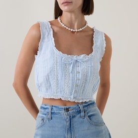 Model wearing LoveShackFancy Blue Finch cotton crop top with lace trim and bow detail, styled with pearl necklace and light wash jeans