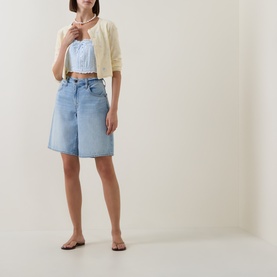 Model wearing LOVESHACKFANCY Blue Finch cotton top, styled with cream cropped cardigan, light wash denim shorts, and flat sandals.