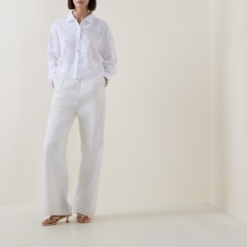 Model wearing LOVESHACKFANCY Optic White linen shirt, styled with wide-leg white trousers and tan strappy heeled sandals.