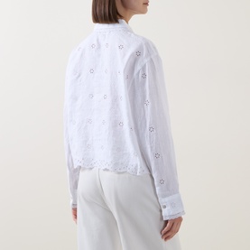 Model wearing LOVESHACKFANCY Optic White linen top with broderie anglaise floral detail and scalloped hem, styled with white trousers