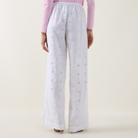 Model wearing LOVESHACKFANCY Optic White linen wide-leg trousers with floral embroidery detail, styled with a pink long-sleeve top. Rear view.