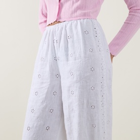Model wearing LOVESHACKFANCY Optic White linen wide-leg trousers with floral broderie anglaise embroidery, styled with a pink knit top.