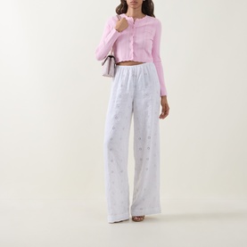 Model wearing LOVESHACKFANCY Optic White linen wide-leg trousers with floral embroidery, styled with a pink cropped cardigan.