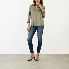Model wearing LAgence Smokey Olive silk blouse with button-front and 3/4 sleeves, styled with blue skinny jeans and black heeled sandals.