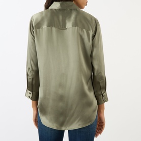 Model wearing LAgence Smokey Olive silk blouse, back view, with rolled cuffs and yoke detail, styled with blue jeans.