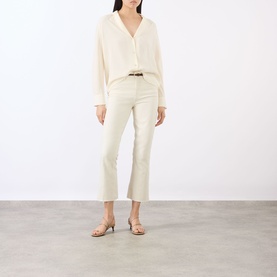 Model wearing L'Agence vintage white flare jeans with cream blouse, brown belt and nude heeled sandals.