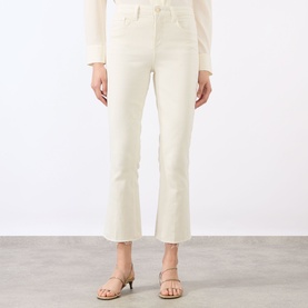 Model wearing LAgence vintage white flare jeans, styled with a cream knit top and nude strappy heeled sandals.
