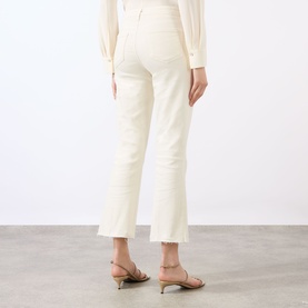 Model wearing LAgence vintage white flare jeans, cropped length with raw hem, styled with beige strappy heels and ivory long-sleeve top.