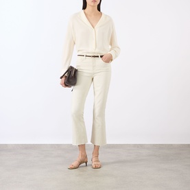 Model wearing LAgence vintage white flare jeans with cream blouse and thin belt, carrying dark brown bag, styled with nude heeled sandals.