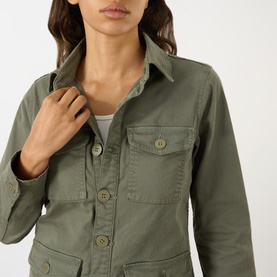 Model wearing LAgence Smokey Olive cotton-linen jacket, close-up detail of chest pockets and button fastening over white top.